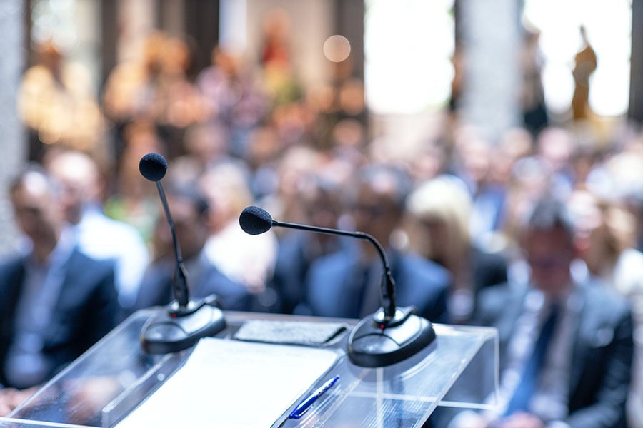 a close-up of microphones on a conference stage with a blurred audience in the background