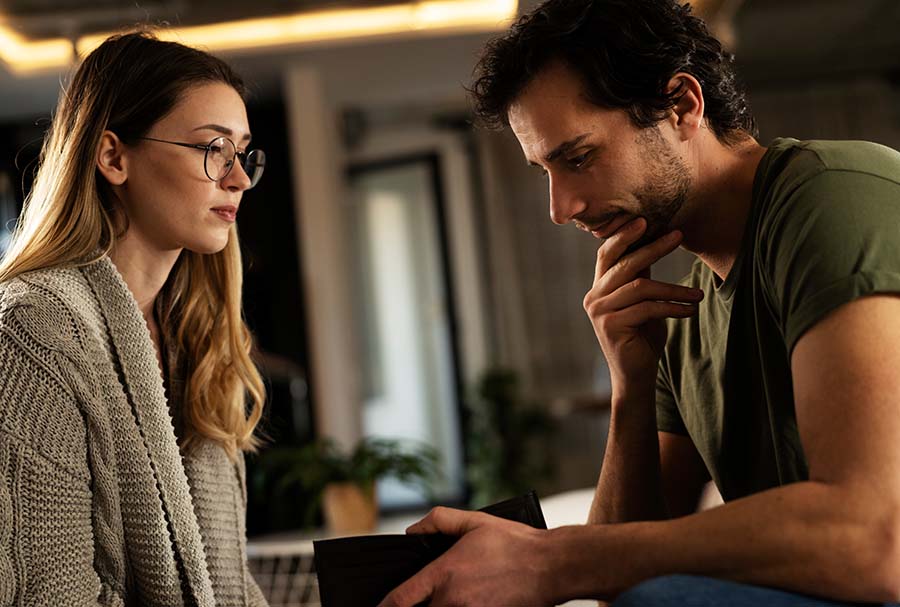 A man looks annoyed while holding a wallet, with a woman looking scared next to him