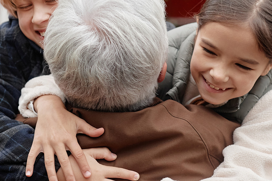 A close up of two very happy children hugging a man, who is seen from behind and has grey hair