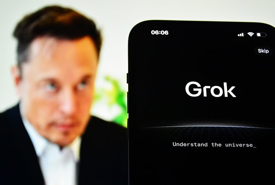 A phone with the grok app on the screen, with Elon Musk in the background