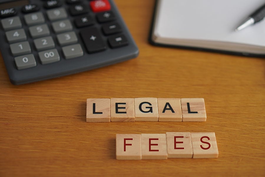 Tiles spelling out 'legal fees' next to a calculator and notepad and pen on a desk