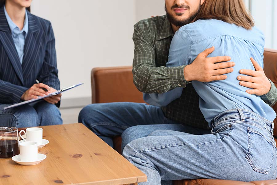 A couple hug, with a therapist looking on