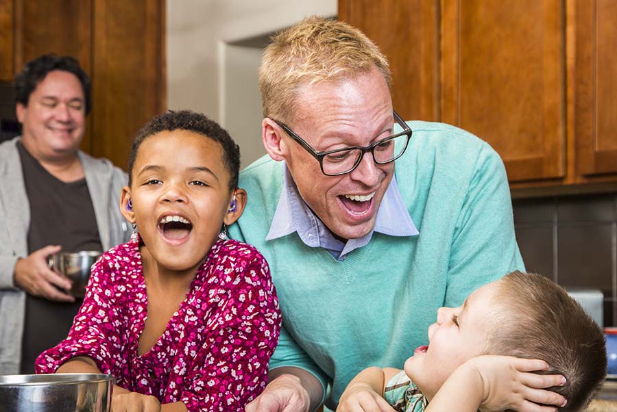A mixed race family with two young children and two dads laughing in the kitchen