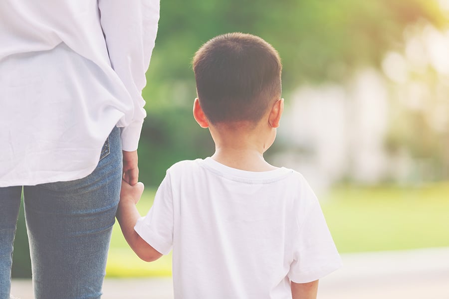 A small boy seen from behind, holding the hand of a woman