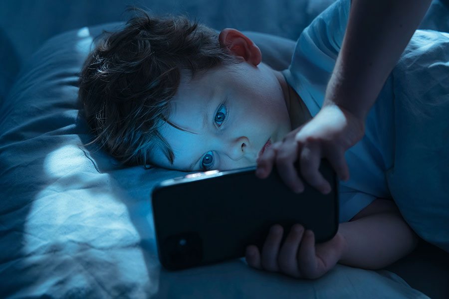 A young boy lies in bed looking at a phone