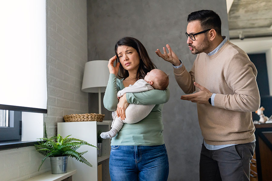 A man gestures angrily towards a crying woman holding a baby