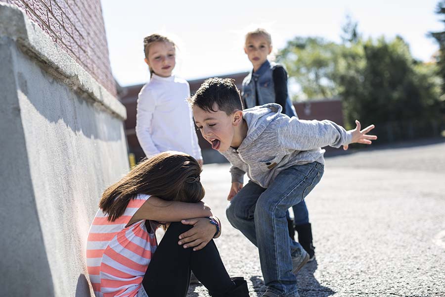 A young girl sits cowering on the floor while a young boy stands over her shouting