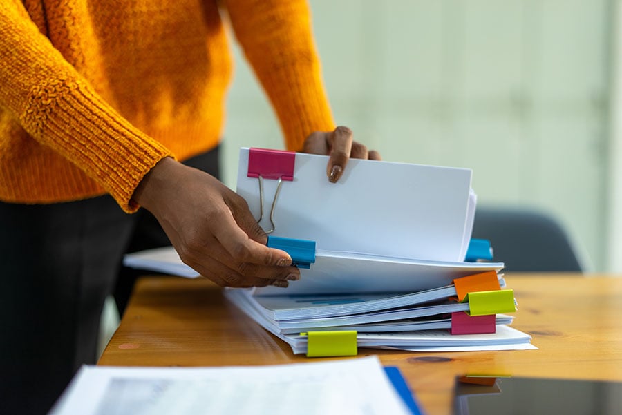 A woman holds a pile of organised papers, separated with large paper clips