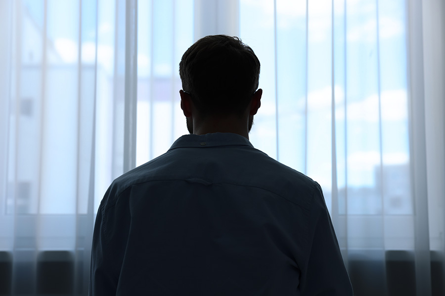 A silhouette of a man sitting along looking out of a window