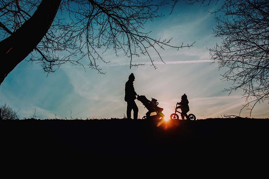 A man with a pushchair and a small child seen in silhouette from a distance