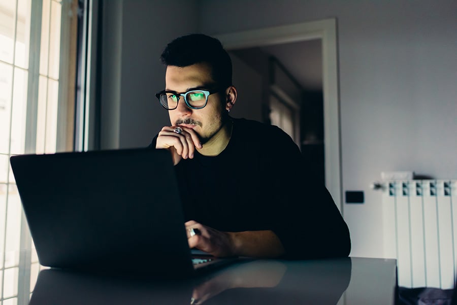 A man in a dimly lit room looks at a laptop screen