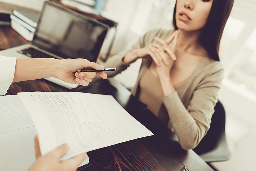 A defiant-looking young woman sits with arms folders while a lawyer hands her papers and a pen