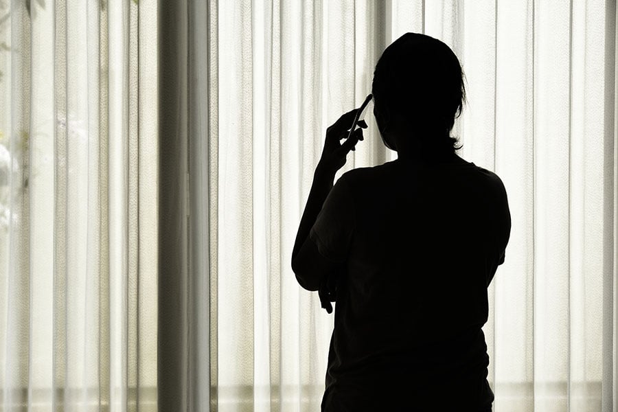 A silhouette of a woman seen from behind as she looks out of a window