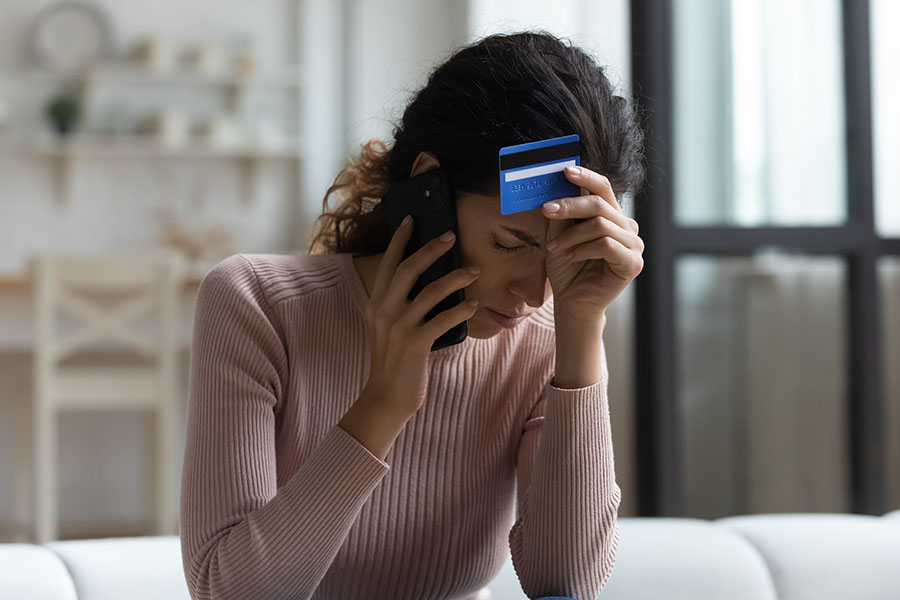 A worried looking woman holds a credit card while speaking on the phone