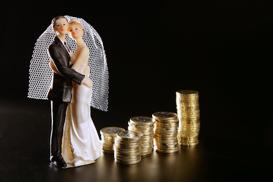 Bride and groom figurines next to piles of gold coins