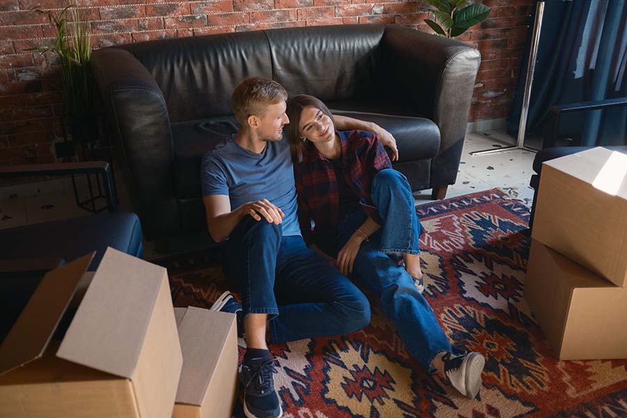 A young couple relax on the floor of a lounge surrounded by empty packing boxes