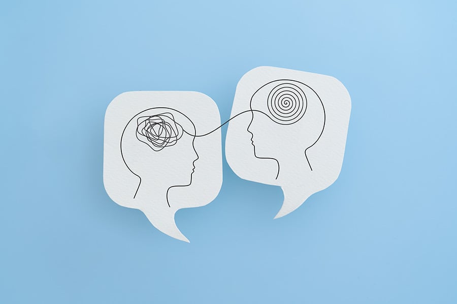 Two speech bubbles with outlines of heads drawn on them, one filled with scribbles the other filled with a neat spiral