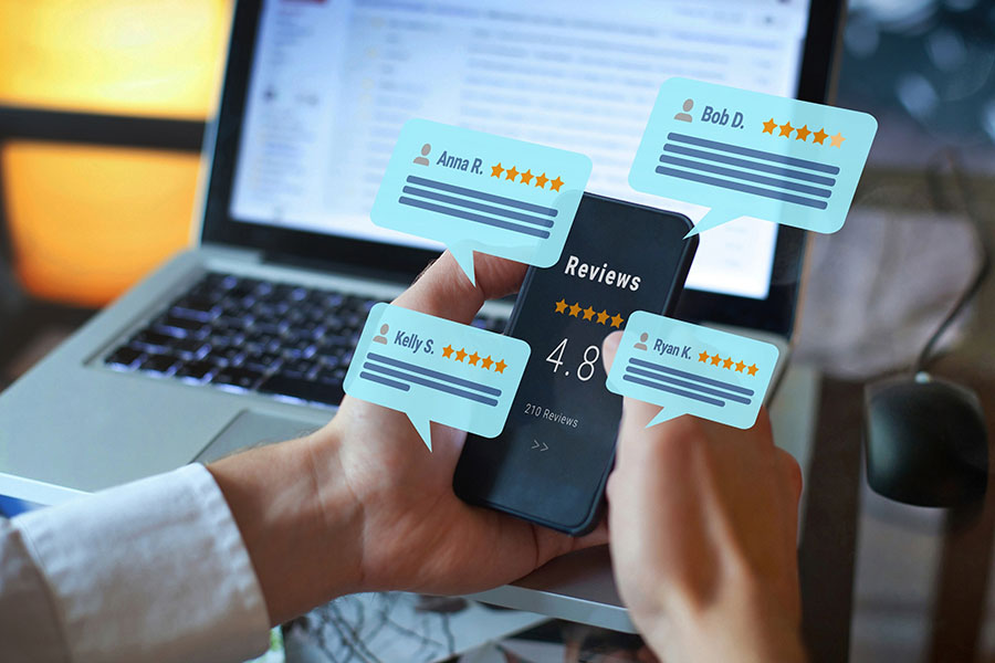 Graphics of speech bubbles with five star reviews over an image of hands holding a mobile phone in front of a laptop