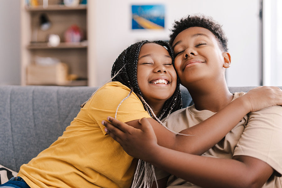 A happy looking brother and sister hug on a sofa