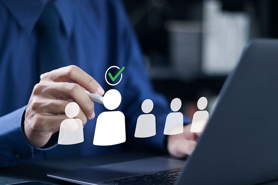 A man using a laptop, overlaid with a graphic of simple people figures, one with a green tick above it