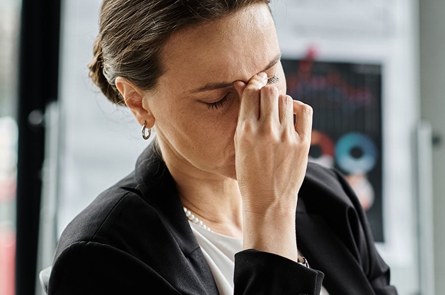 A stressed looking smart woman in a black suit rubbing her eyes