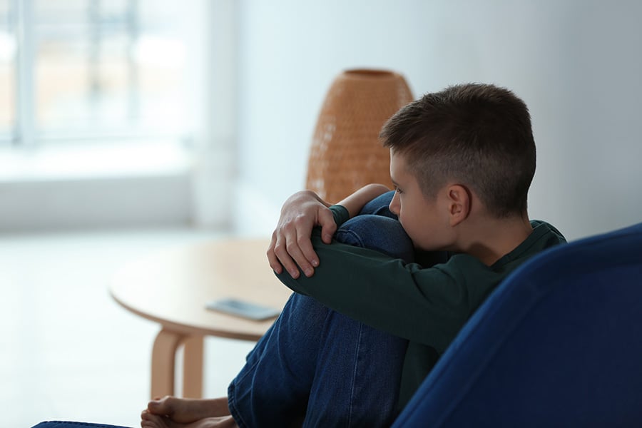 A teenage boy sits alone looking sad in an empty room