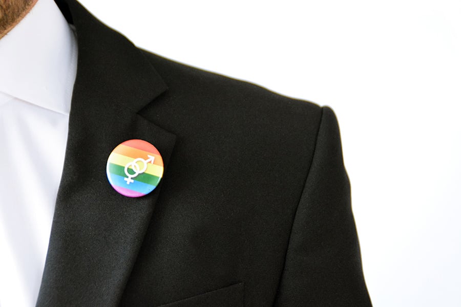 An LGBTQ pin on the lapel of a black suit