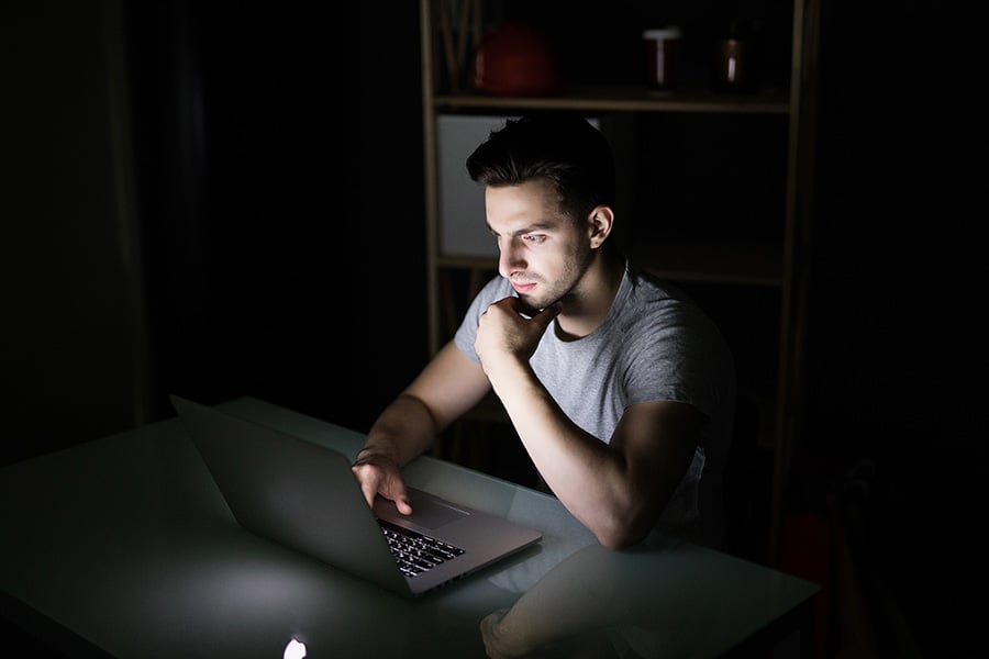 An angry looking man using a laptop in a dark room
