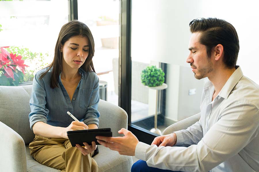 A smiling man watches a sad looking woman digitally sign a tablet