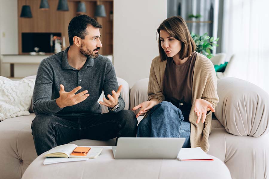 A frustrated couple on the sofa with a laptop, calculator and sheets of paper on the table in front of them