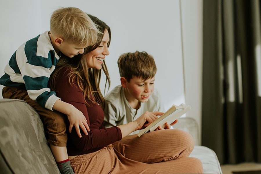 A woman is reading to two young boys on a sofa