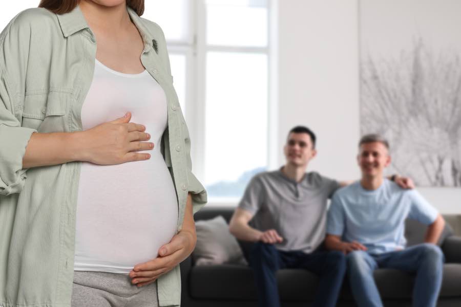 Two men on a couch in the background with a pregnant woman in the foreground