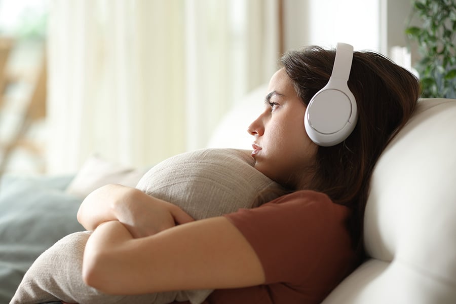A sad-looking teen girl sits on a sofa hugging a cushion