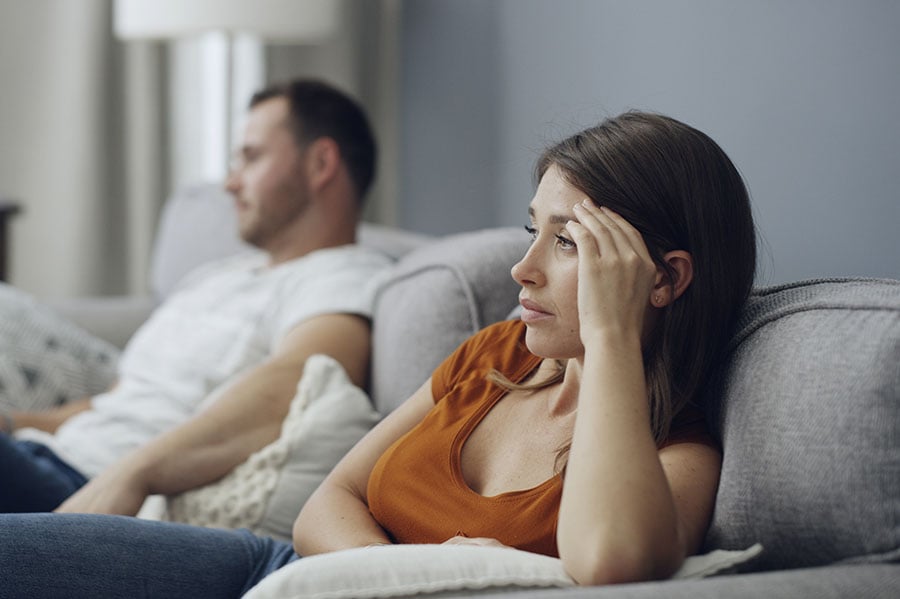 A sad looking woman on the sofa, with a happier looking man next to her