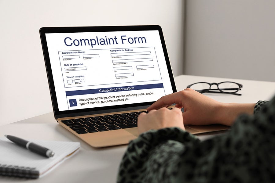 Hands typing on a laptop which has a complaint form on the screen