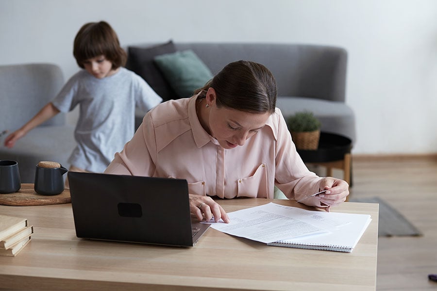 mother sat at table paying bills, with child playing in background