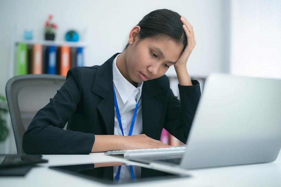 A woman at her desk with her head in her hand looking stressed and unhappy